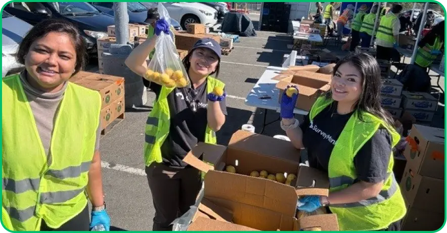 Three SurveyMonkey employees smiling and wearing safety vests outside and packing boxes